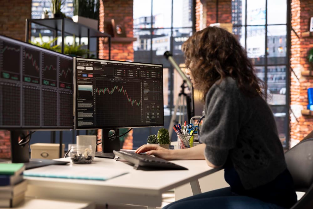 Trader trabajando en un escritorio con varias pantallas en una oficina luminosa